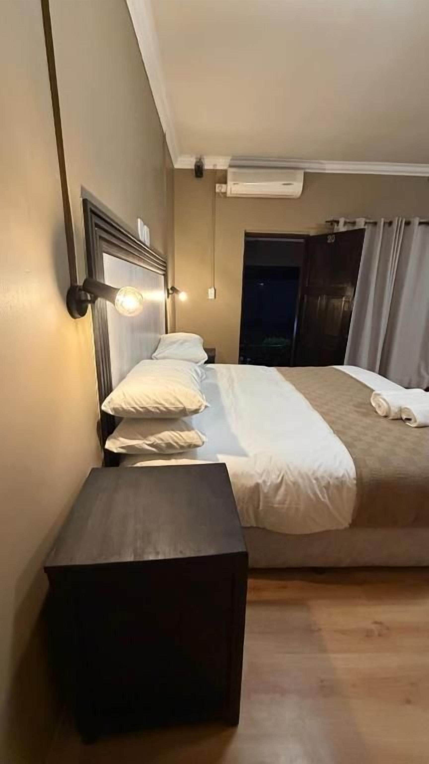 Una habitación de hotel con una cama, mesita de noche y una lámpara de pared.