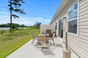 Une terrasse avec une table et des chaises, une poubelle et un bâtiment doté d’une fenêtre et d’une porte.