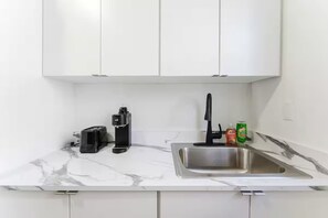 Eine Küche mit weißen Schränken, einer Marmorarbeitsplatte, einer Kaffeemaschine, einer Spüle und einer Geschirrspülmittel-Flasche.
