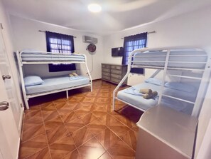 Ein Zimmer mit zwei Etagenbetten, Holzboden, Fernseher und einem kleinen Schrank.