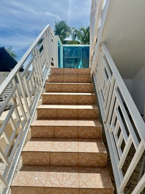 Eine Treppe im Freien mit geometrischem Muster, gesäumt von weißen Geländern, die zu einer Glastür führt.