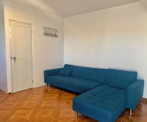 Ein Zimmer mit einem petrolfarbenen Sofa, einer weißen Tür und einem Bild von Segelbooten an der Wand.