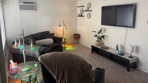 A living room with a sofa, a glass coffee table, a floor lamp, a TV, and a wall-mounted shelf. - Welcome to Mountain Mist Lodge! (Fort Collins)