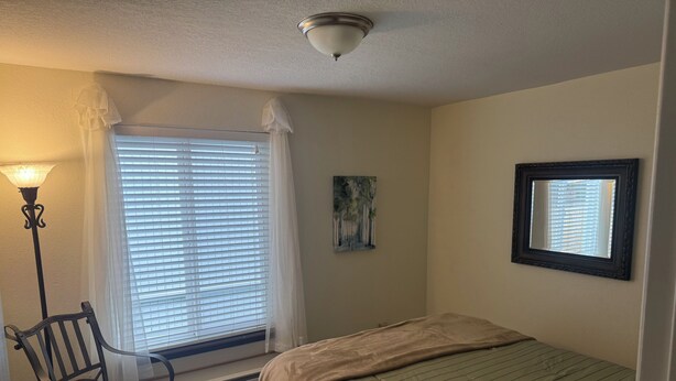 A bedroom with a bed, a chair, a lamp, a window with blinds, and a painting on the wall. - Welcome to Mountain Mist Lodge! (Fort Collins)