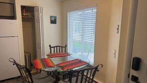 A compact kitchen with a dining table, chairs, a refrigerator, and a window with blinds. - Welcome to Mountain Mist Lodge! (Fort Collins)