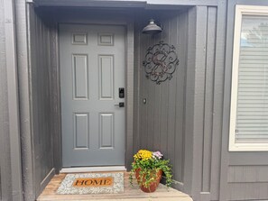 A gray door with a doormat labeled 'HOME' and a potted plant with yellow and purple flowers.