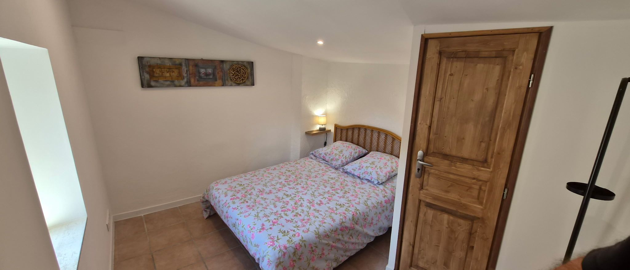 Une chambre à coucher avec un lit, une table de chevet, une œuvre d’art murale et une porte en bois.