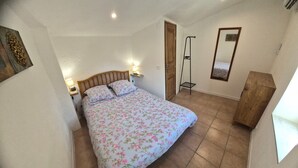 A bedroom with a bed, bedside lamps, a wooden wardrobe, a mirror, and a door. - Village house for 5 people. (Peyruis)