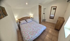 A bedroom with a bed, bedside lamps, a wooden wardrobe, a mirror, and a door. - Village house for 5 people. (Peyruis)