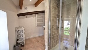 A bathroom with a glass shower enclosure, a white wicker drying rack, and a tiled floor. - Village house for 5 people. (Peyruis)