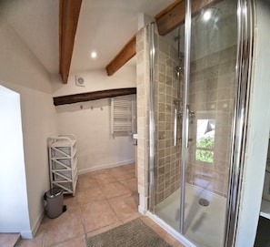 A bathroom with a glass shower enclosure, a white wicker drying rack, and a tiled floor. - Village house for 5 people. (Peyruis)