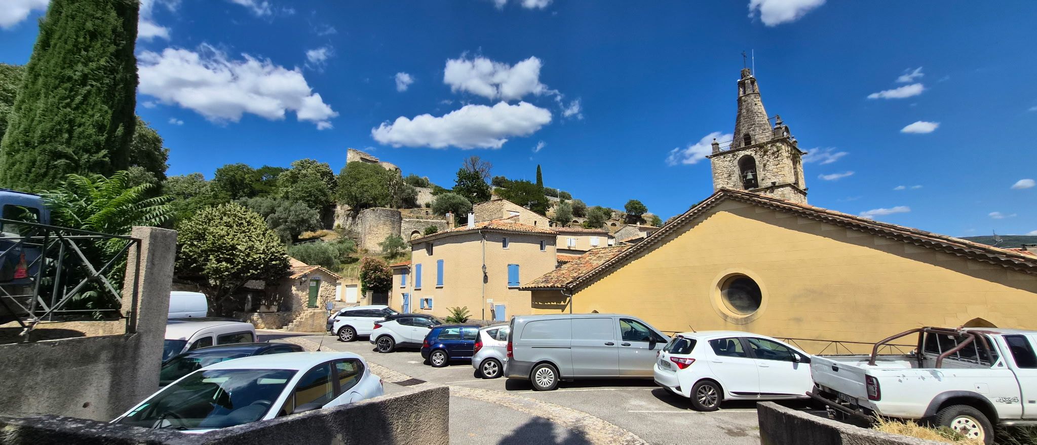 Un estacionamiento con varios autos, una iglesia con un campanario y edificios de arquitectura tradicional.