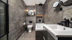 A modern bathroom with a white bathtub, a toilet, and a sink area with toiletries.