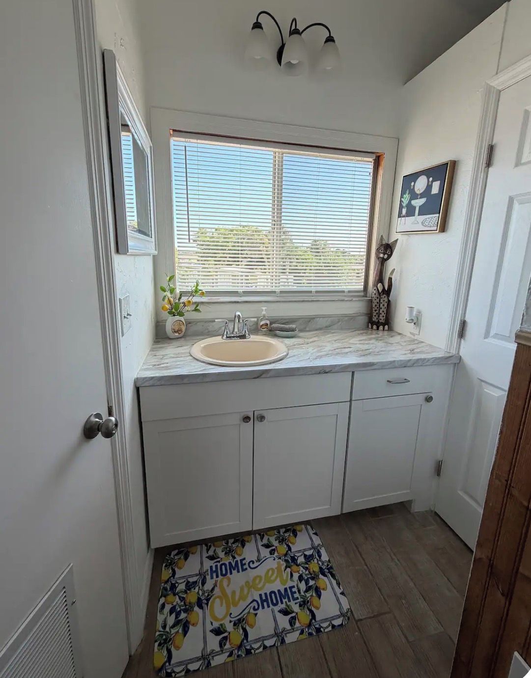 Baño con lavamanos, tocador y ventana con persianas.