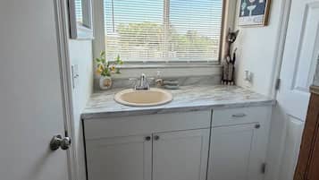 Baño con lavamanos, tocador y ventana con persianas.