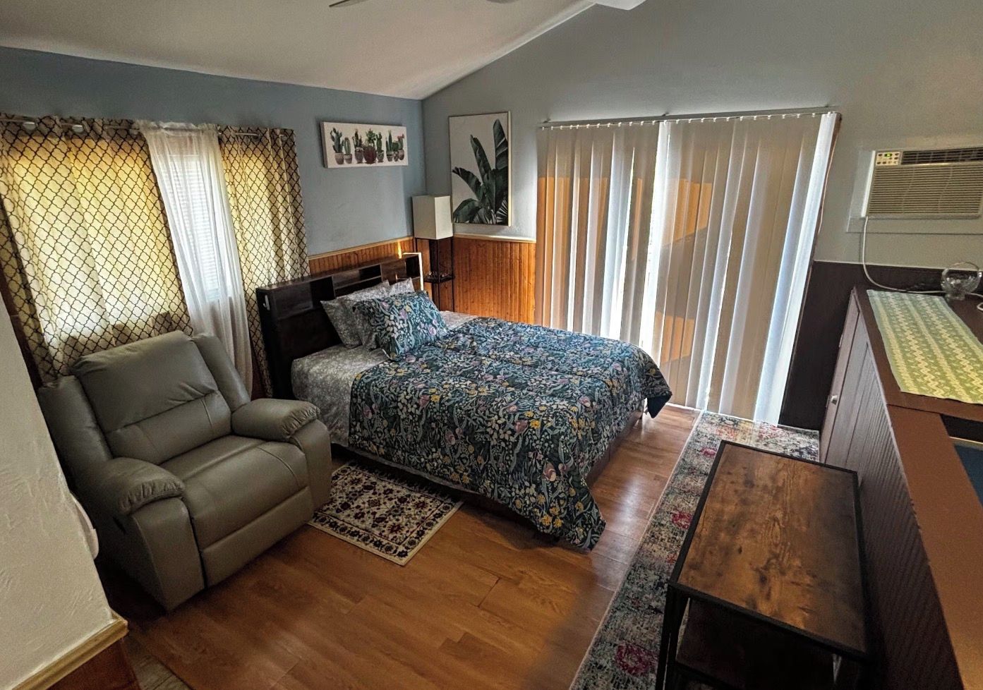 Un dormitorio con cama, sofá, escritorio y ventana con cortinas.