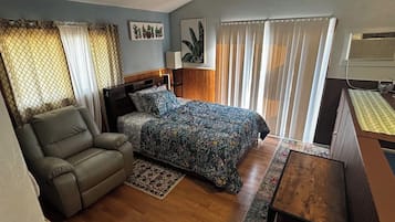 Un dormitorio con cama, sofá, escritorio y ventana con cortinas.