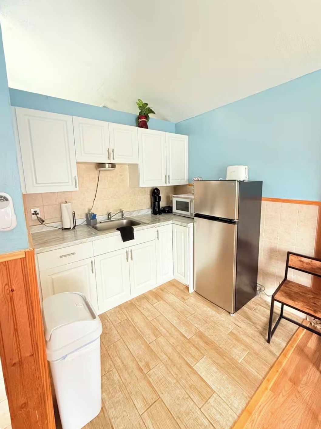 A compact kitchen with white cabinets, a stainless steel refrigerator, a microwave, and a coffee maker.