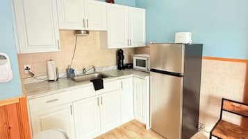 A compact kitchen with white cabinets, a stainless steel refrigerator, a microwave, and a coffee maker.
