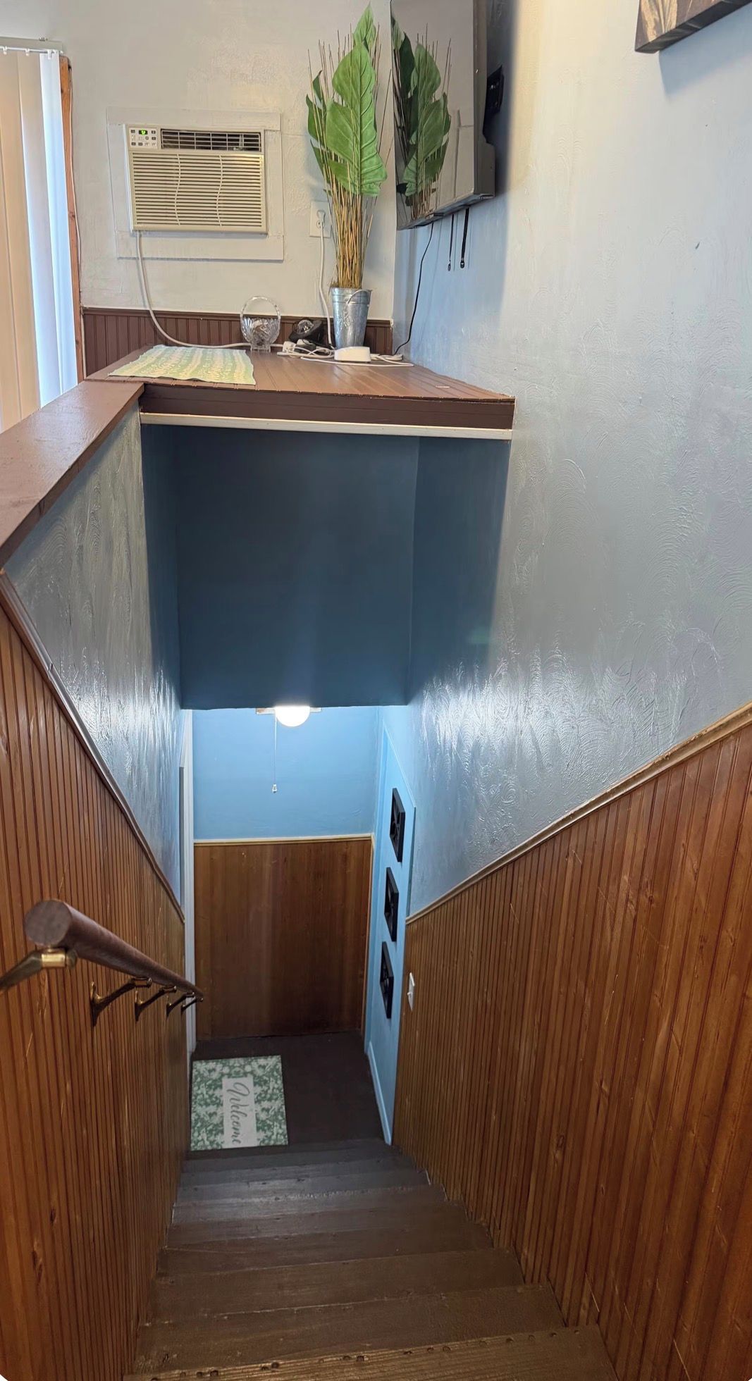 A wooden staircase with a blue wall and a small rug at the bottom.