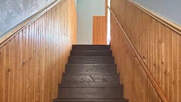 A wooden staircase with a handrail, leading to a landing with a light blue wall and a vent.