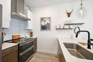 A modern kitchen with a stainless steel sink, a built-in oven, and a marble countertop.