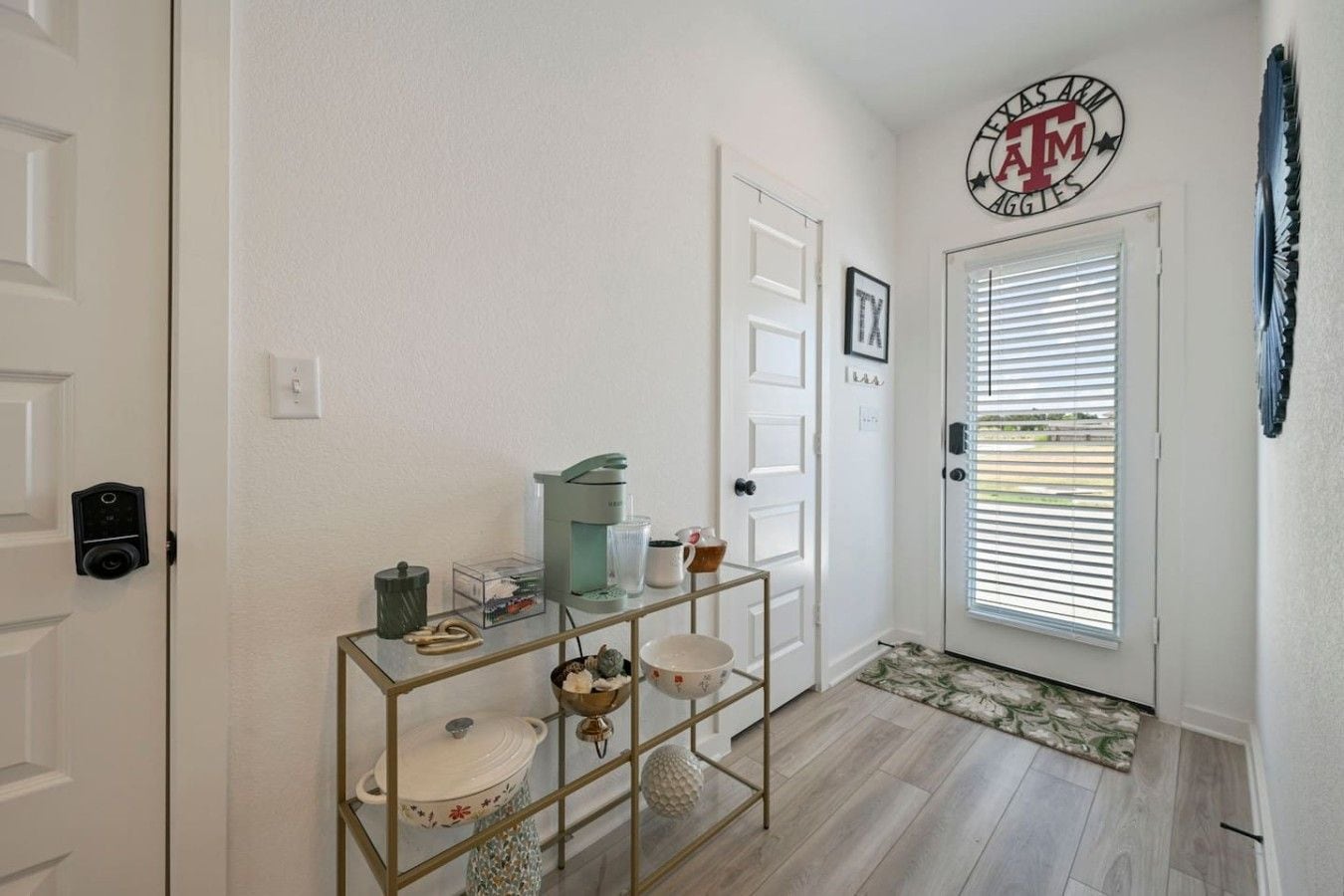 A hallway with a door, a coat rack, a coffee maker, and a framed picture.