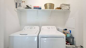 A laundry area with two front-loading washing machines, a shelf with various items, and a whiteboard on the wall.