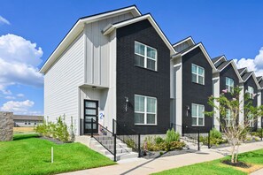 A row of modern apartment buildings with a uniform architectural style, featuring a combination of white and dark siding, large windows, and a well-maintained lawn. - Pristine New 2BR Townhome | South College Station (College Station)
