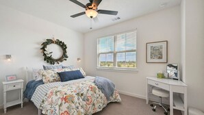 Quarto com cama, escrivaninha, ventoinha no teto, janela e luminária na parede.