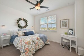 A bedroom with a bed, a desk, a ceiling fan, a window, and a wall-mounted light fixture. - Pristine New 2BR Townhome | South College Station (College Station)