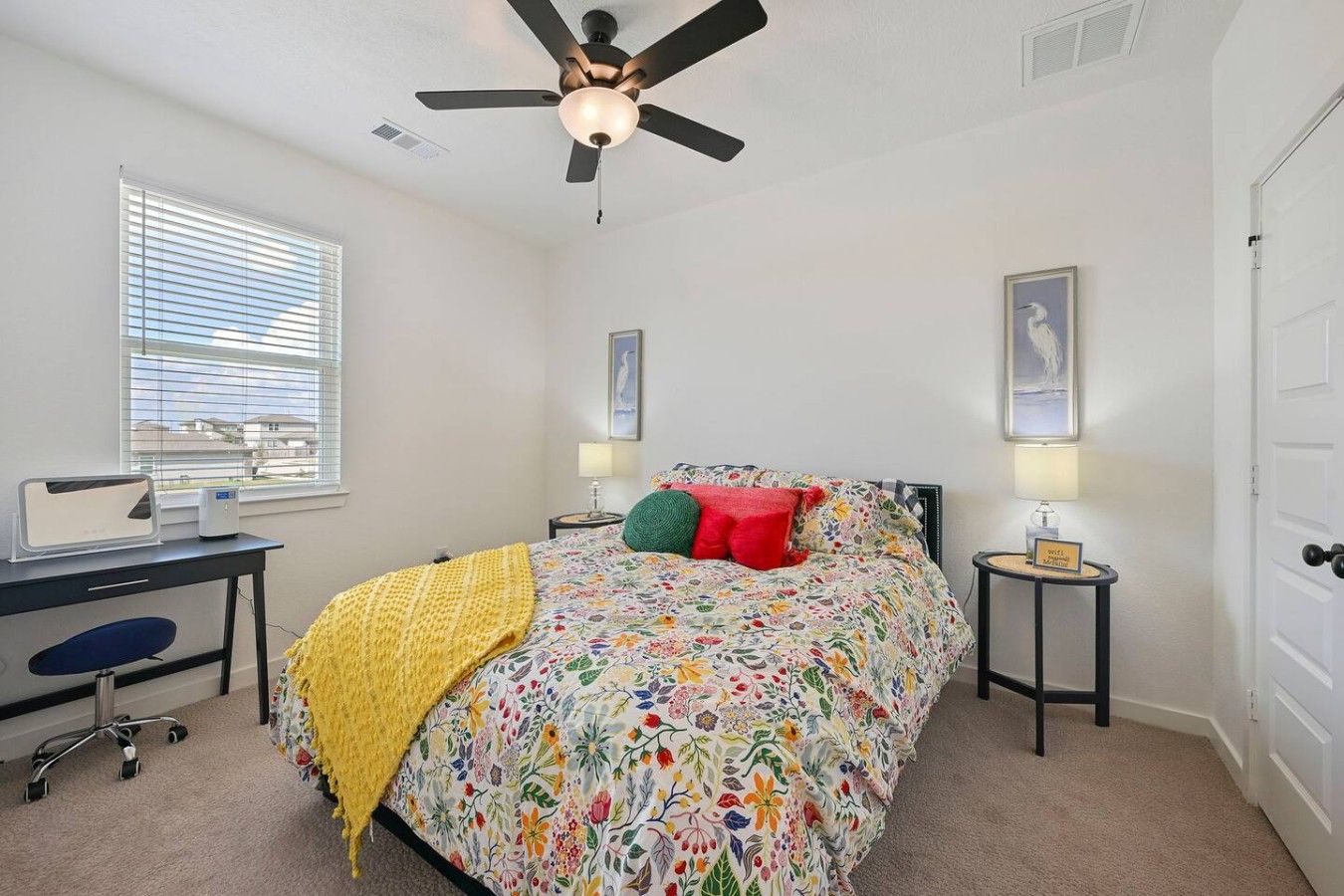 A bedroom with a bed, a desk, a chair, a ceiling fan, and a window with blinds.