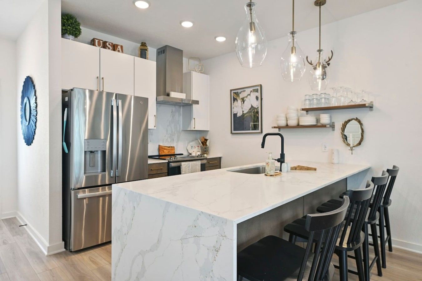 A modern kitchen with a marble island, stainless steel appliances, and pendant lighting.