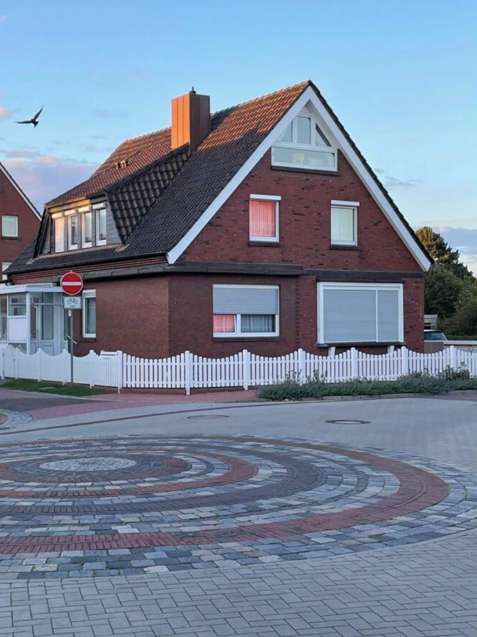 A two-story house with a red brick exterior, a white fence, and a circular driveway.