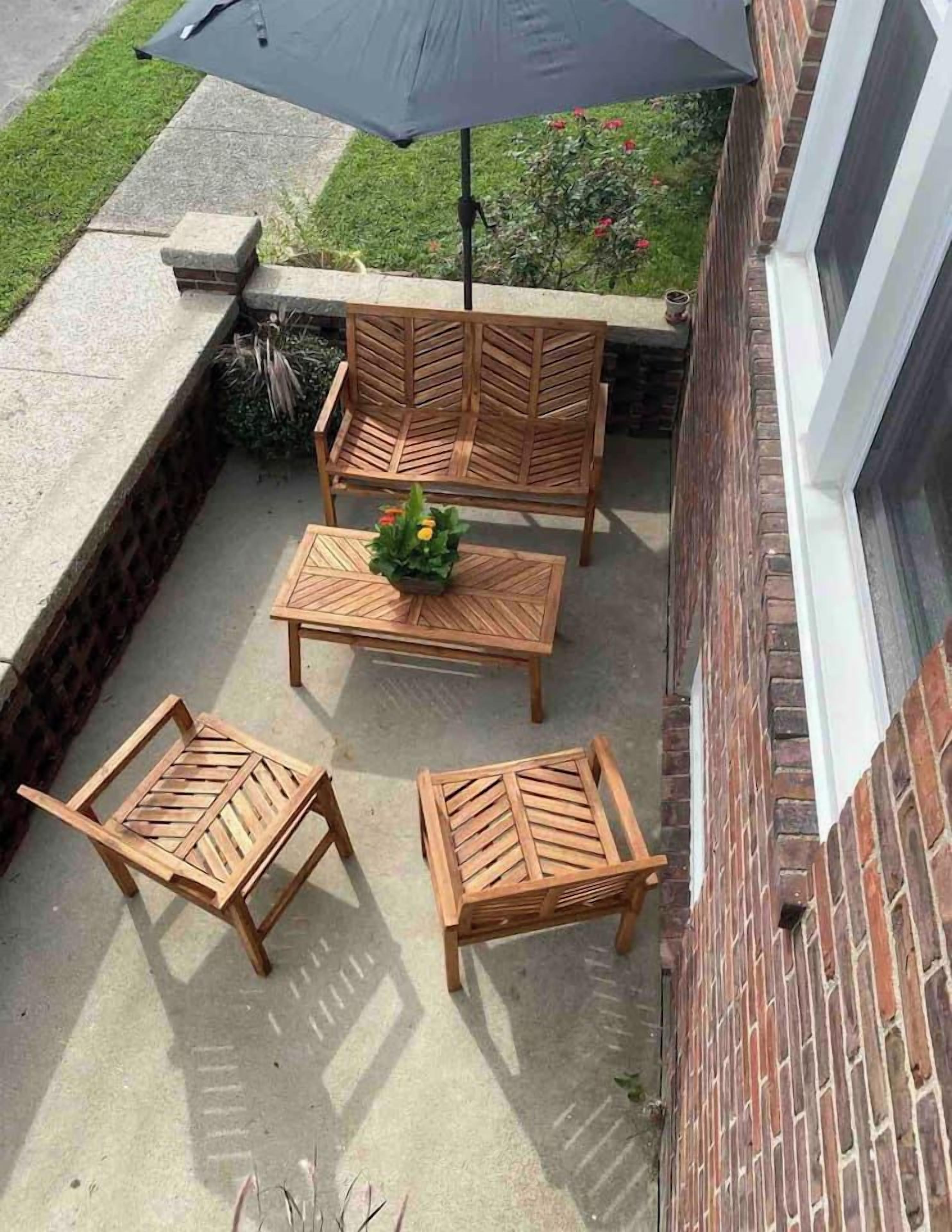An outdoor patio with a table and four chairs, a large umbrella, and a brick wall.