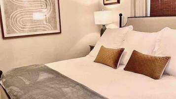 A hotel room with a bed, a framed artwork, a nightstand, a lamp, and a window with curtains.