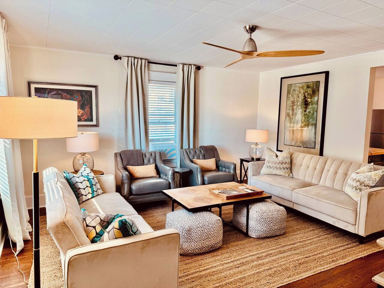 A modern living room with a sofa, chairs, ottomans, a coffee table, and a ceiling fan.