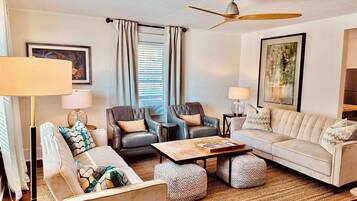 A modern living room with a sofa, chairs, ottomans, a coffee table, and a ceiling fan.