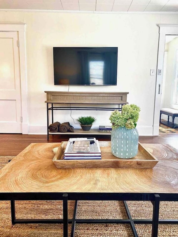 Un salon avec un téléviseur à écran plat fixé au mur, une table basse en bois avec un plateau et un vase décoratif.
