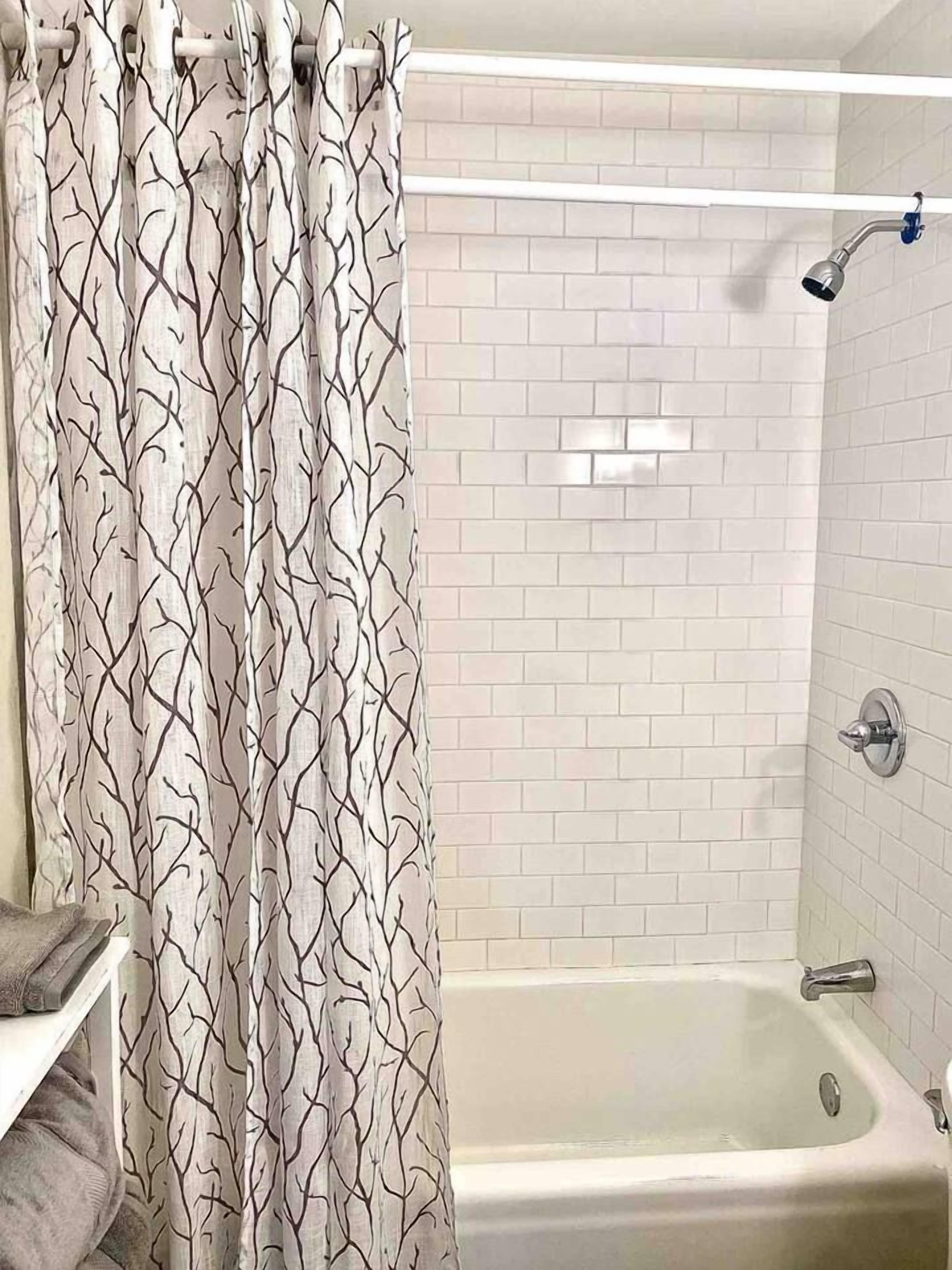 A bathroom with a shower, a bathtub, and a curtain with a tree pattern.