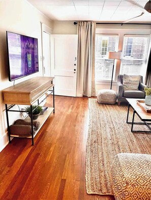 Un salon avec un plancher en bois, un téléviseur posé sur un meuble, un canapé, une table basse et un tapis à motifs.