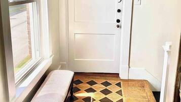 Un pasillo estrecho con una puerta blanca marcada con el número 3, un banco y un piso con diseño.