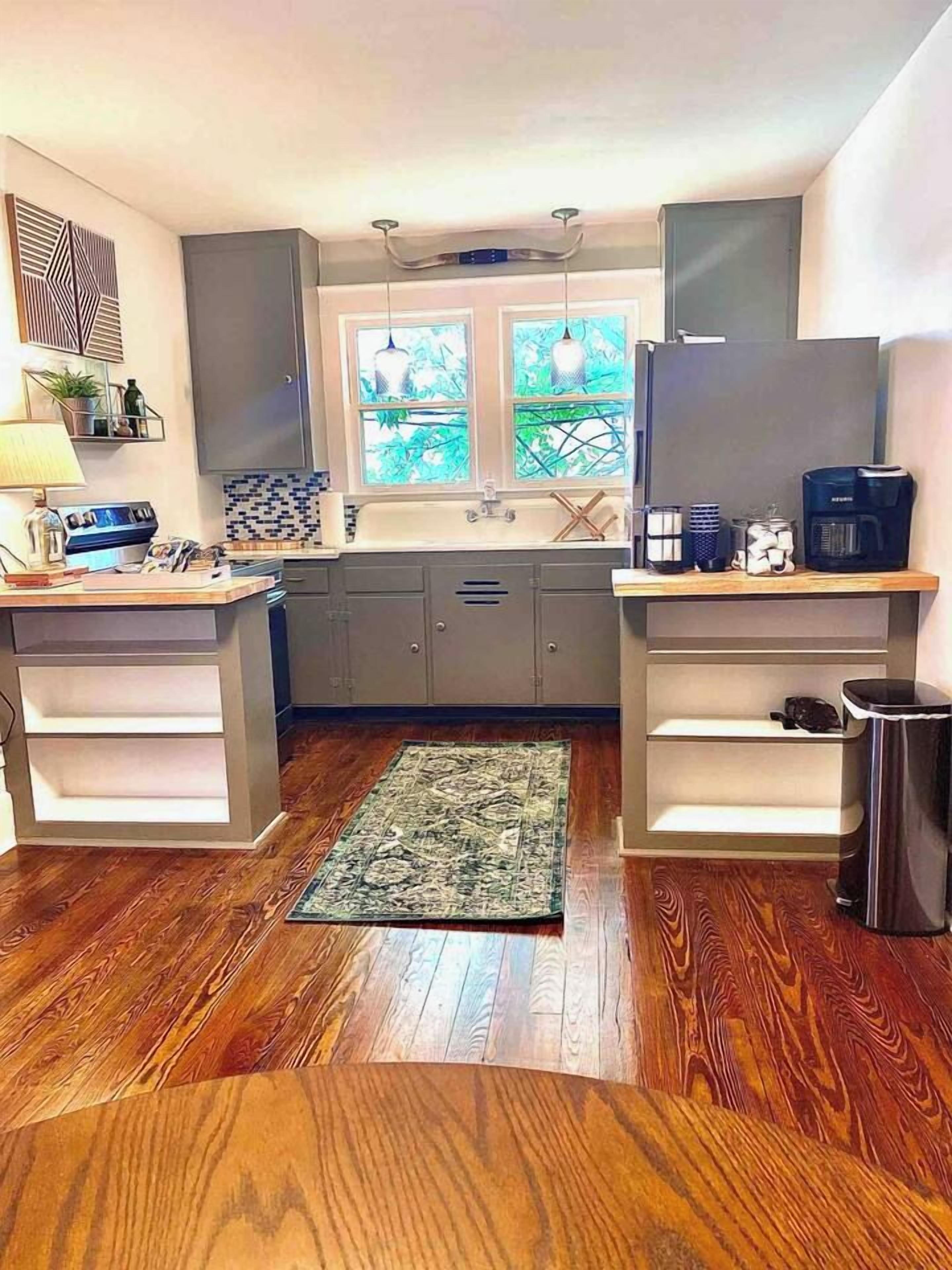 A modern kitchen with grey cabinets, a wooden floor, a window with a view, and a coffee machine.