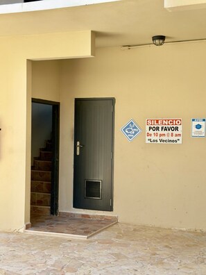 A building entrance with a closed door, a staircase leading inside, and two signs on the wall indicating noise restrictions. - Bright Coastal Stay Near Beach w/ Pool & Tennis (Boquerón)