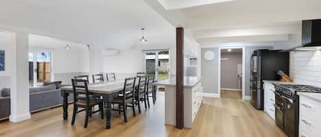 A modern kitchen with a central island, a dining area with a wooden table and chairs, and a living room with a sofa and a TV.