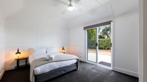 Un dormitorio con una cama, dos lámparas de noche, un ventilador de techo y un ventanal corredero que da a un área exterior.