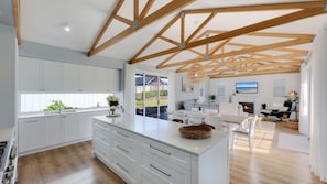 A modern kitchen with white cabinetry, a large island, and a dining area with a fireplace. - Diana's Joy - Luxury, Space, Golf & Coastal Living in Warrnambool (Warrnambool)