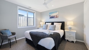 A bedroom with a bed, a chair, a nightstand, a lamp, and a window. - Diana's Joy - Luxury, Space, Golf & Coastal Living in Warrnambool (Warrnambool)