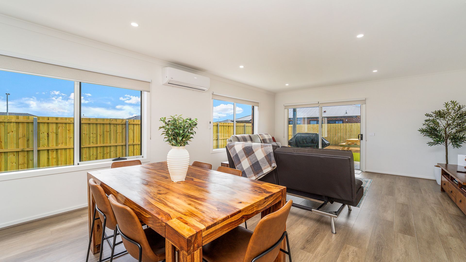 A spacious room with a wooden dining table, comfortable seating, a sofa, and a view of the backyard through large windows.
