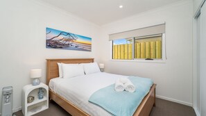 A bedroom with a bed, a painting, a window with a view, and a bedside table with a lamp. - Woonan - Modern and designed with families in mind (Warrnambool)